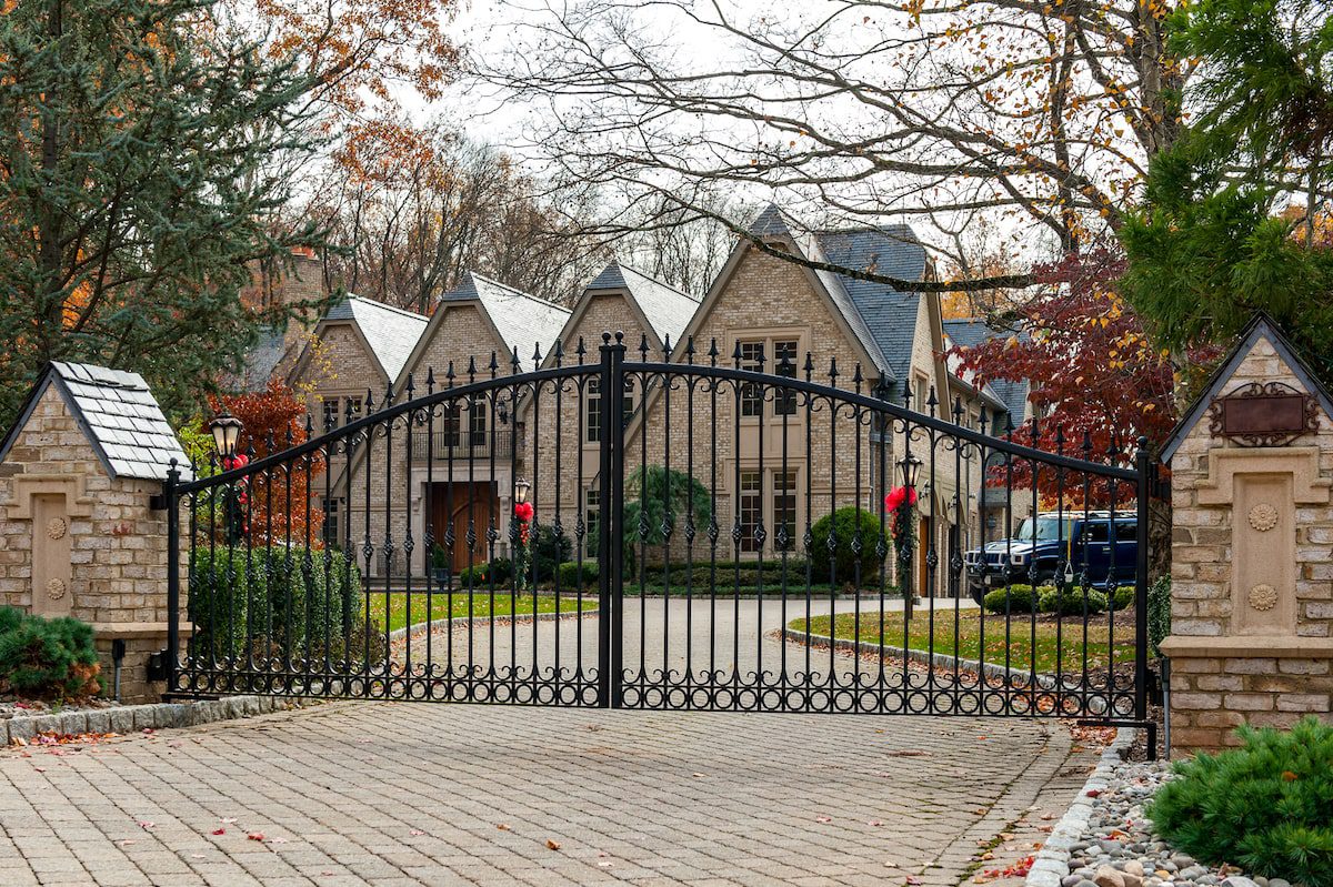 The wrought iron automatic driveway gate in this photo sits between two columns that echo the design of the home behind them.