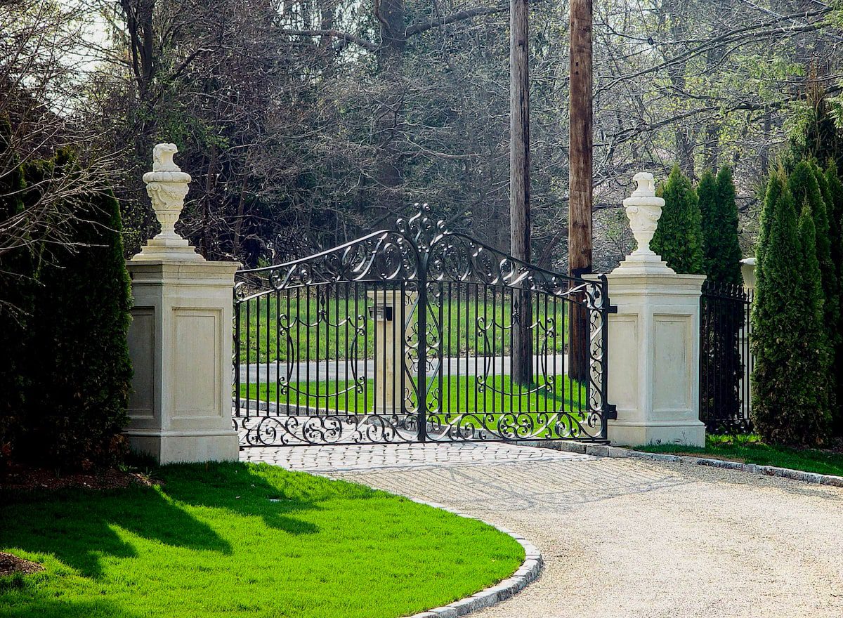 An ornate wrought iron gate sits between two tall limestone columns with decorative sculptures on top. The effect is imposing.