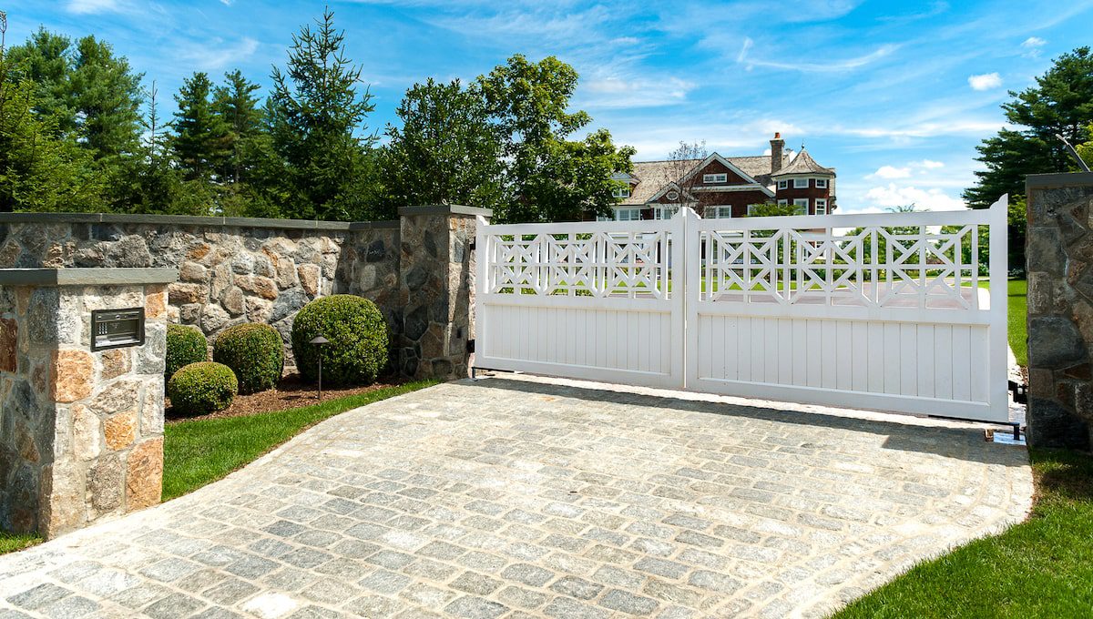 An automatic driveway gate made from wood painted white works with tall stone walls to keep the home in the distance secure.