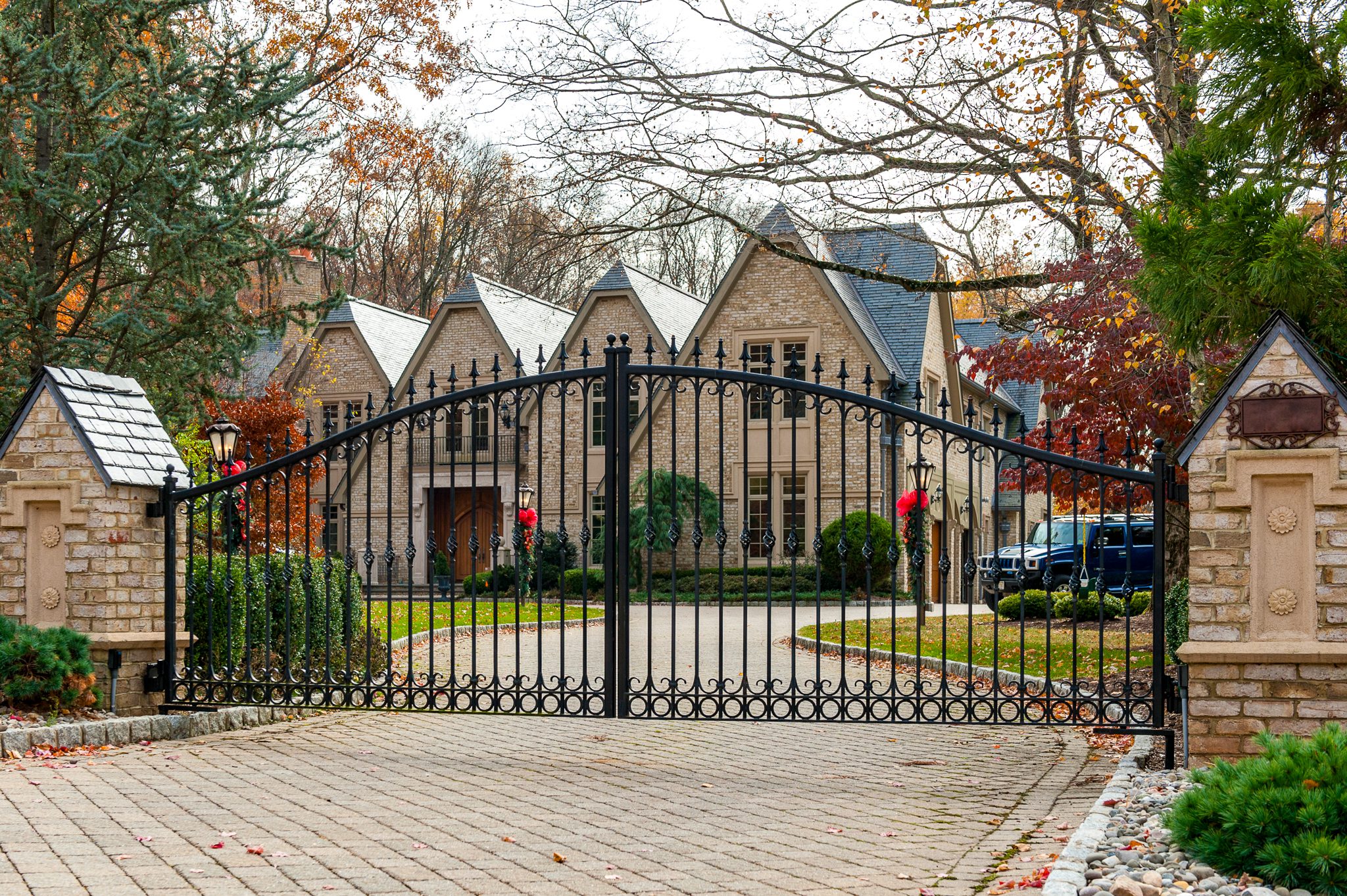 A wrought iron gate with circles along the bottom and finials at the top of each picket stands in front of a home.