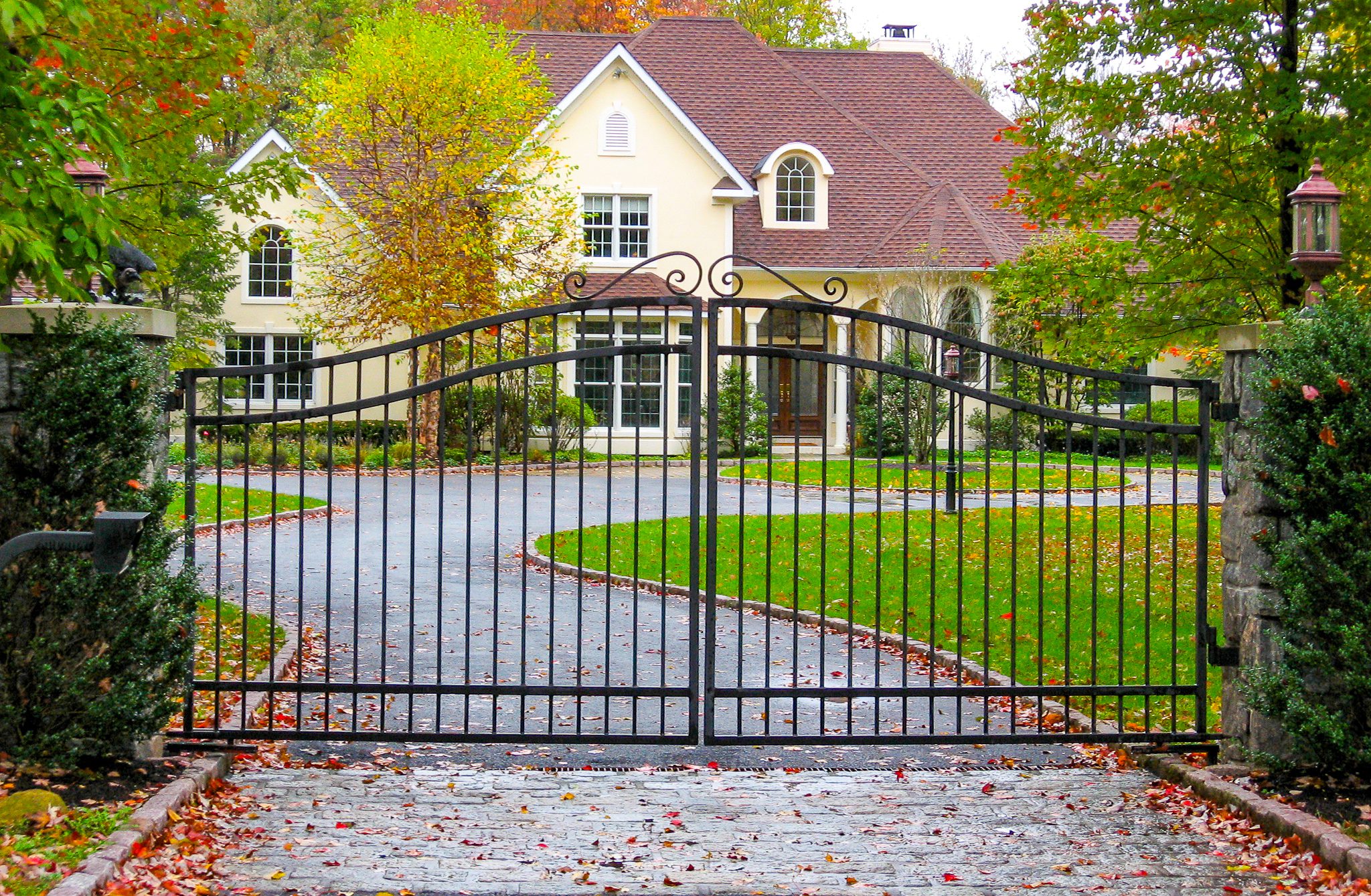 A clean, simple wrought iron gate with an arched top rail stands in front of the driveway to a home.