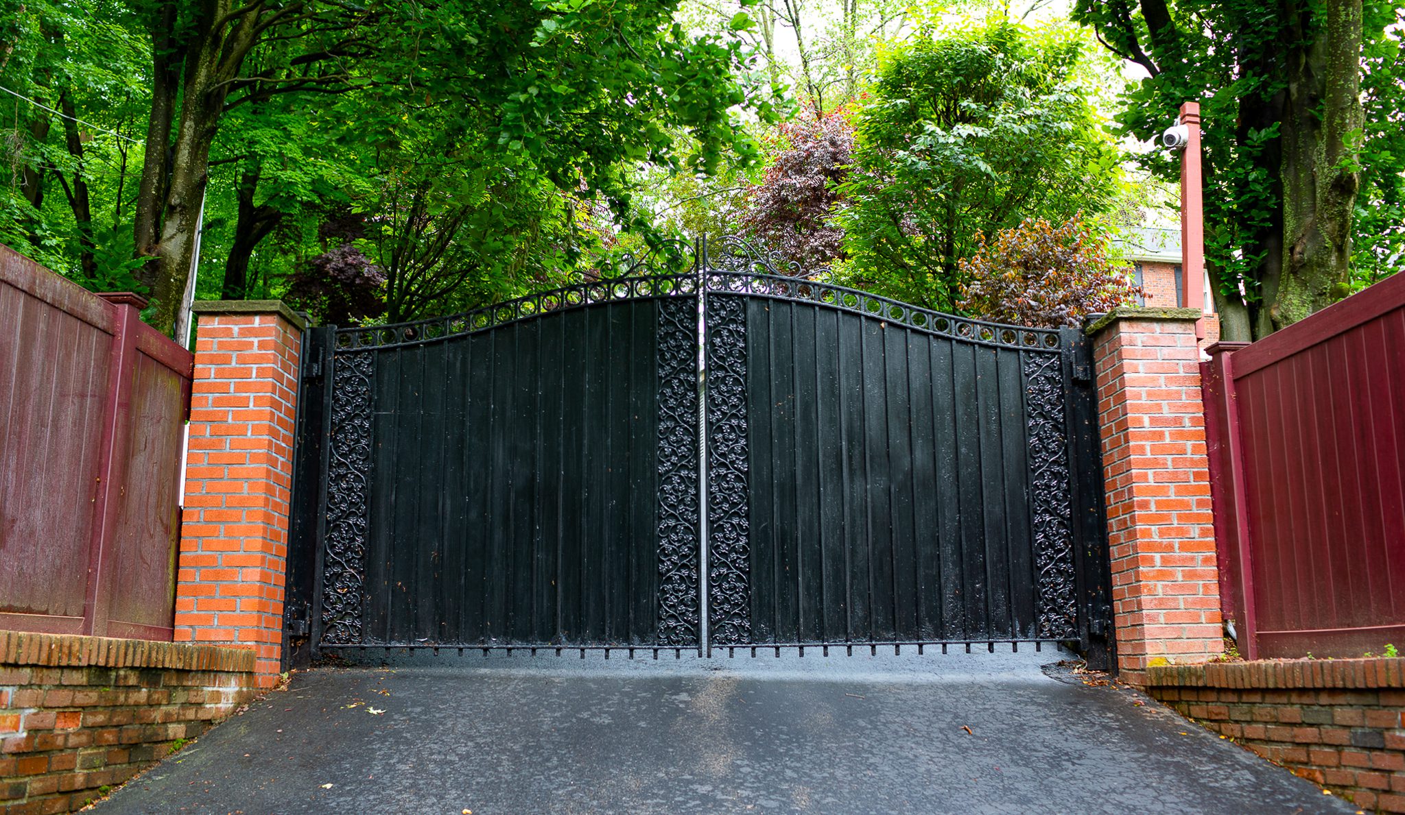 The solid black panels of a wrought iron gate stand between two red brick columns.