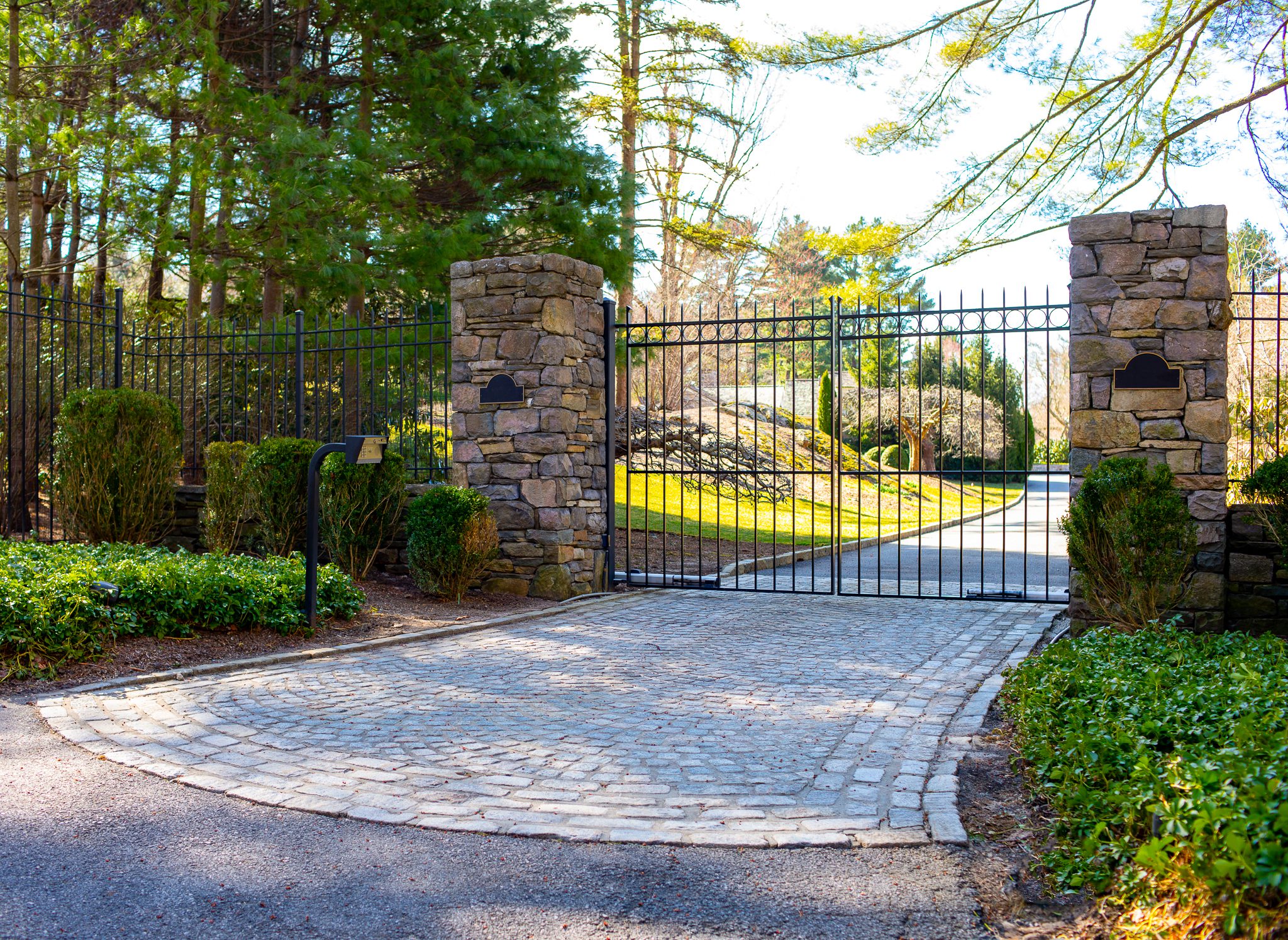 A tall modern-looking wrought iron gate stands between two tan-colored stone columns.