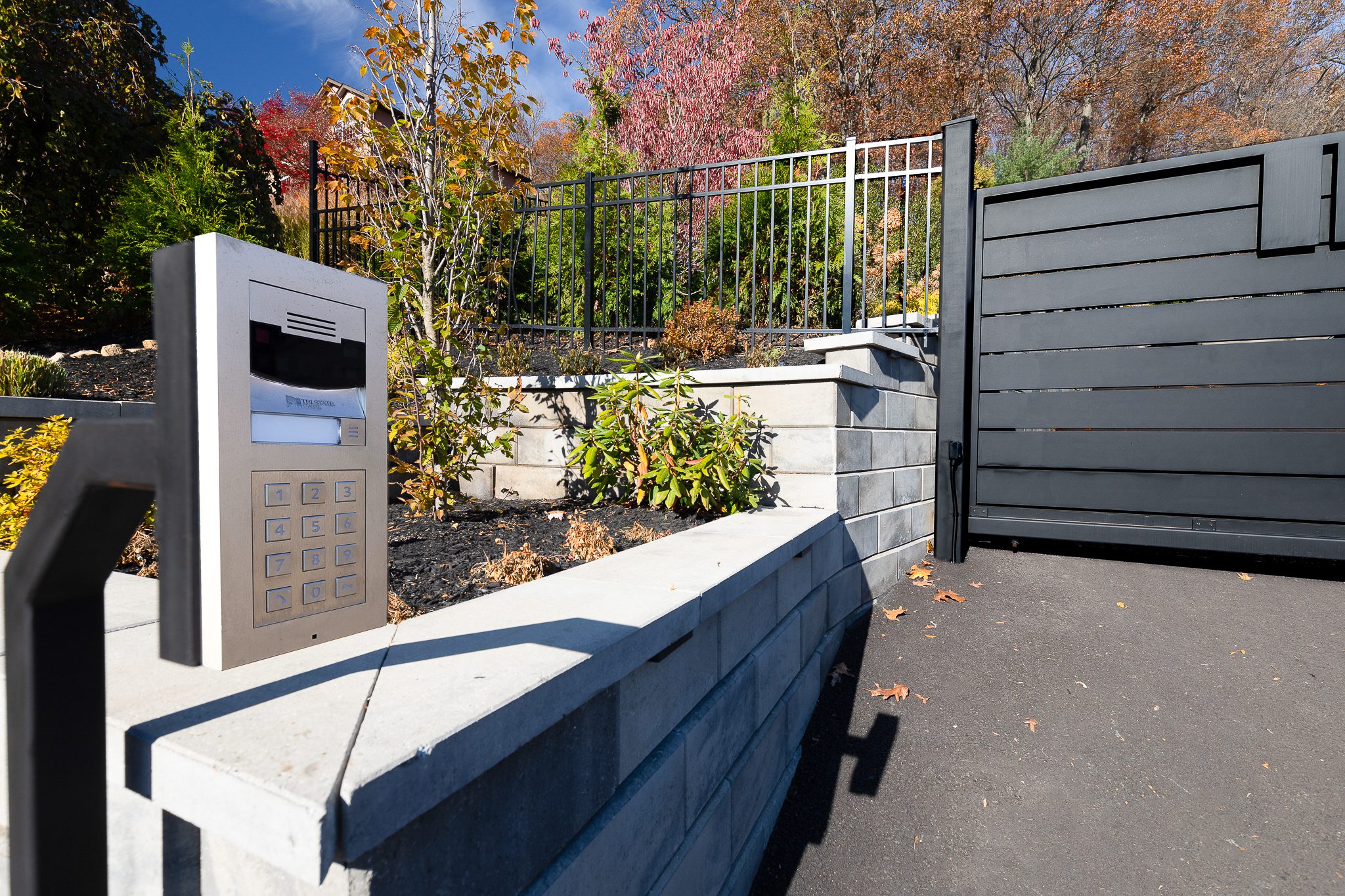 A callbox with a keypad is in the foreground of the photo. In the background is an automatic driveway gate that slides open to allow vehicles to pass up the hill to the home above.